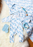 Baby onesie with blue and white pattern, socks, and teething ring on a soft surface