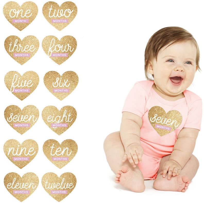 Baby in a pink onesie with 'seven months' printed on it, surrounded by heart-shaped milestone stickers.