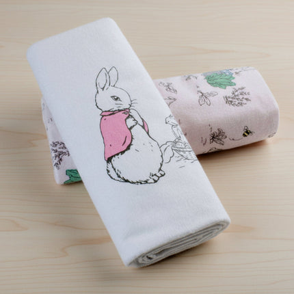 Two folded towels with a flopsy rabbit design and nature-themed pattern on a table background