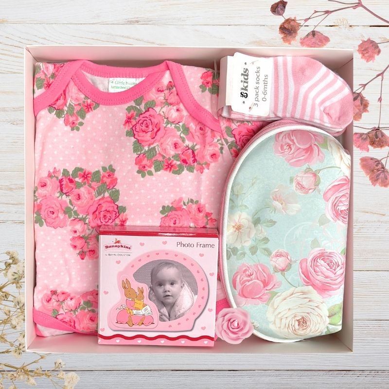 Baby gift set with floral-themed items in a box on a wooden surface.