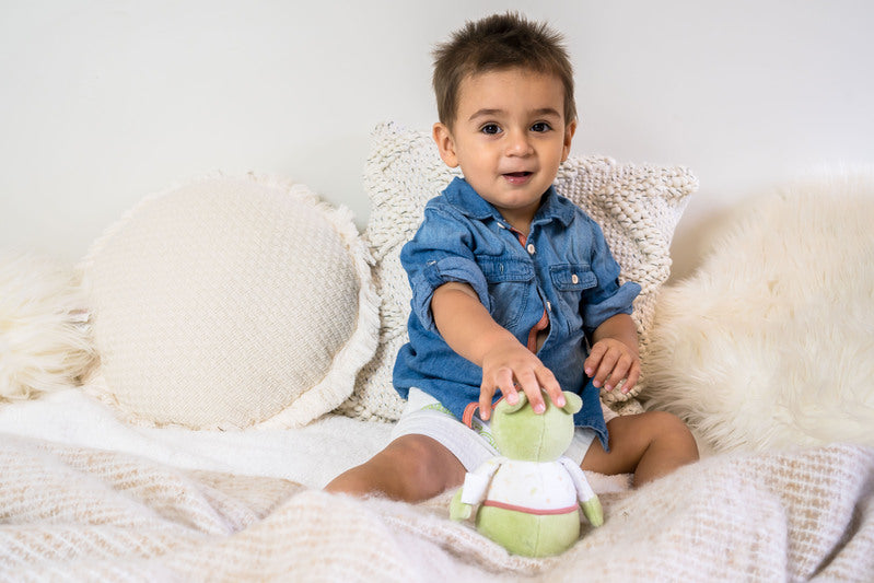 Child sitting on a soft surface holding a green plush toy