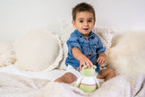 Child sitting on a soft surface holding a green plush toy