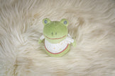 Green frog plush toy on a fluffy white surface