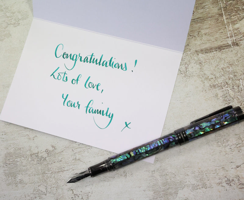 Greeting card with 'Congratulations! Lots of love, Your family x' text and a decorative pen on a textured surface.