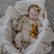 Baby in a beige outfit with a bow, surrounded by soft textures and colors.