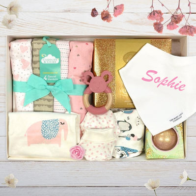 Baby gift set with blankets, a teether, and a bib on a wooden surface.