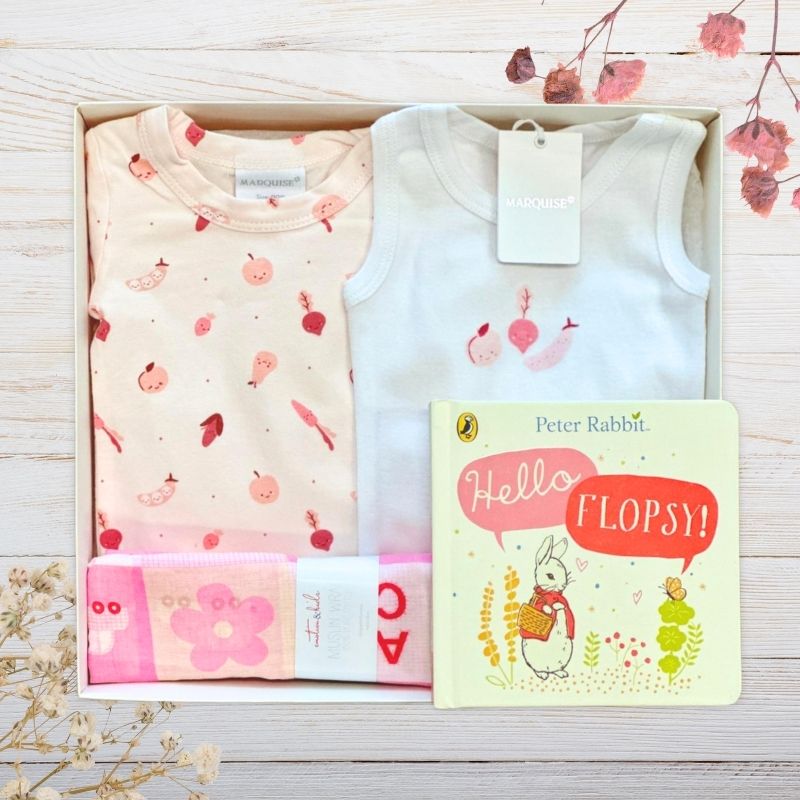 Two baby outfits and a book titled 'Hello Flopsy' on a wooden surface with floral decorations.