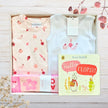 Two baby outfits and a book titled 'Hello Flopsy' on a wooden surface with floral decorations.