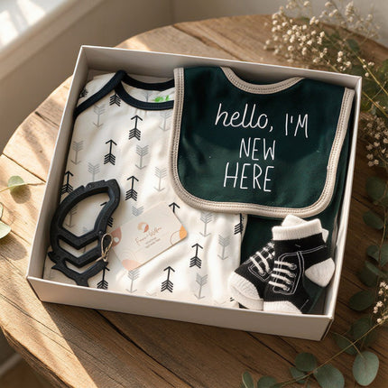 Black and white themed baby baby gift box with clothes and Hello I'm New Here baby bib on a wooden surface