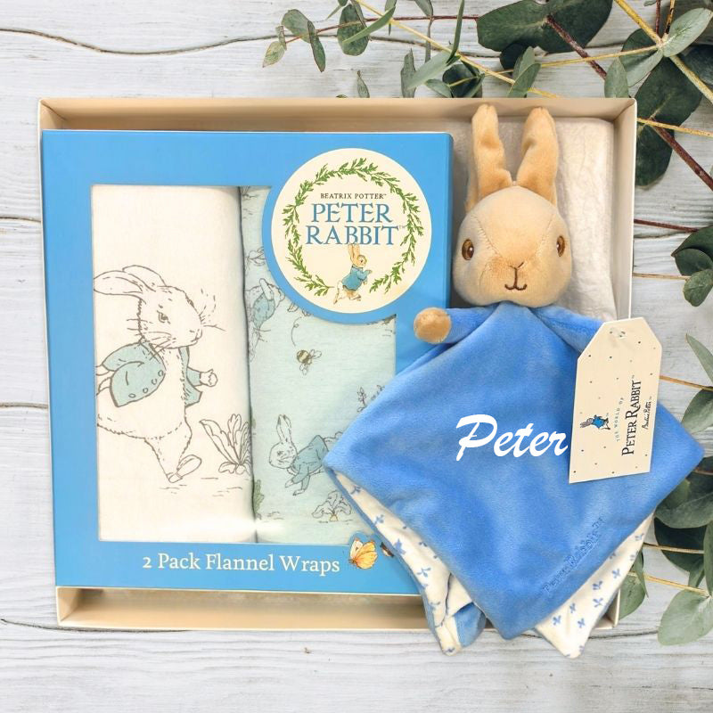 Peter Rabbit plush toy with flannel wraps in a baby gift box on a wooden surface with greenery.