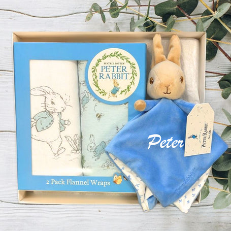 Peter Rabbit plush toy with flannel wraps in a baby gift box on a wooden surface with greenery.
