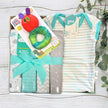 Baby gift set with clothes, toys, and a book in a box on a wooden surface.