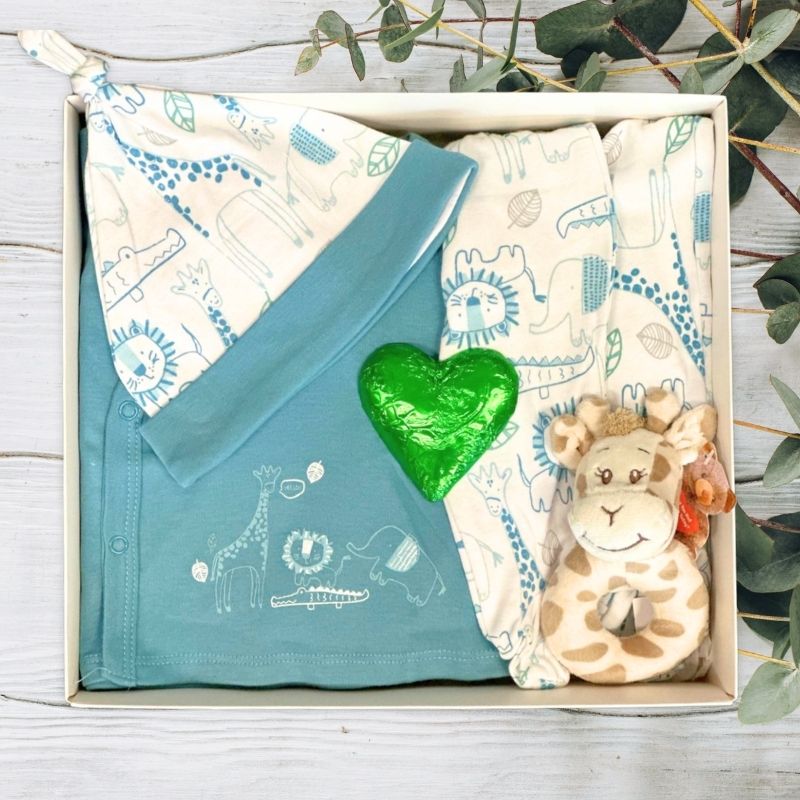 Baby gift set with blanket, heart-shaped item, and soft toy in a box on a wooden surface.