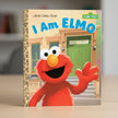 Book cover of 'I Am Elmo' from Sesame Street with Elmo waving in front of a house.