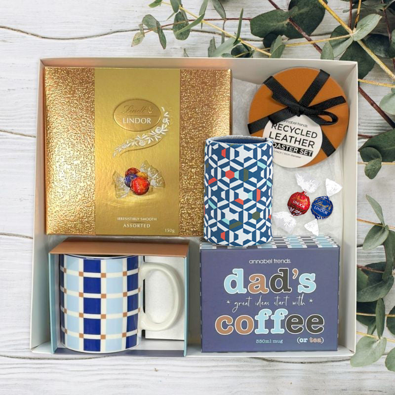 Gift set with mugs, cookies, and a coaster on a wooden surface with greenery.