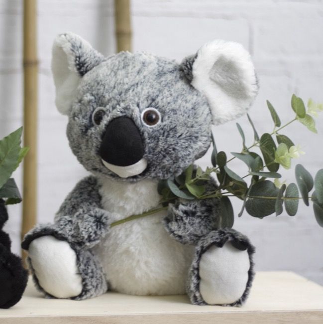 Plush koala toy holding a branch with leaves on a light surface.