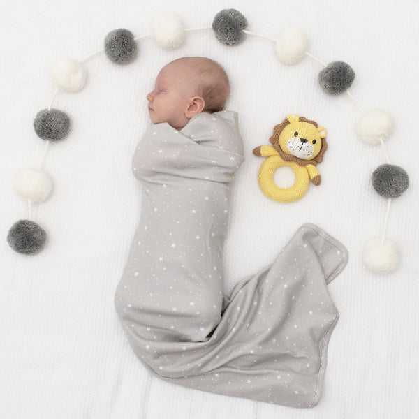Newborn baby wrapped in a gray swaddle with a lion toy on a white background