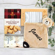 Gift set with Mac's shortbread fingers, a plush toy, and a personalized blanket on a wooden surface.