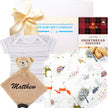 Baby gift set with baby clothes, plush toy, and cookies on a white background
