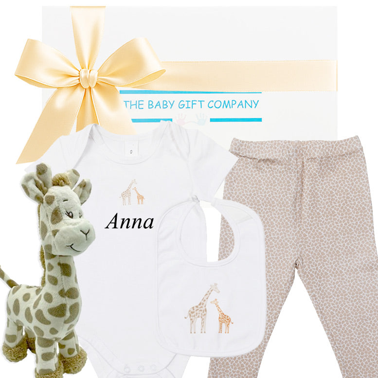 Baby gift set with white shirt, pants, and plush giraffe toy, branded 'The Baby Gift Company'.