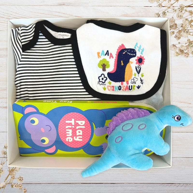 Baby gift box with bib, onesie, teether, and plush toy on a wooden surface.