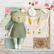 Gift set with plush rabbit toy, baby clothes, and Milk Chocolate Speckle in a gift box on a wooden surface.
