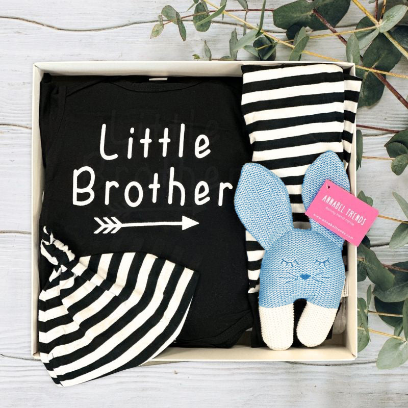 Baby Gifts Box containing a black 'Little Brother' onesie, striped pants, and a plush toy with a plant in the background.