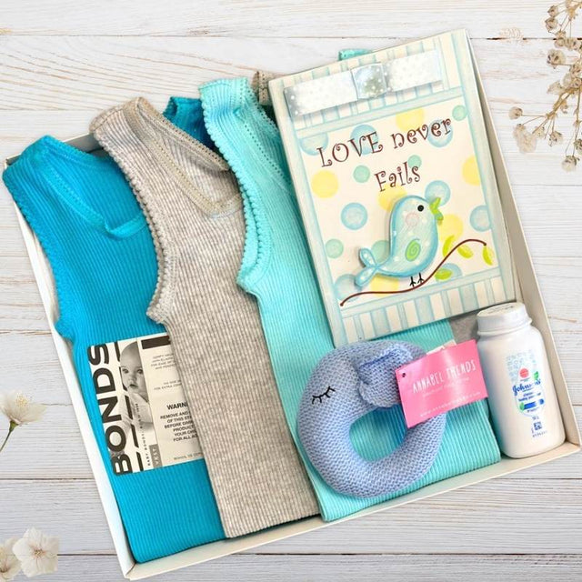 Baby gift set with boys clothes, an elephant blue toy, and a nursery plaque in a gift box on a wooden surface.