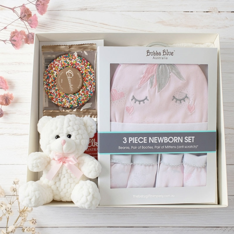 Baby gift set with teddy bear, booties, and hat in a box on a wooden surface.