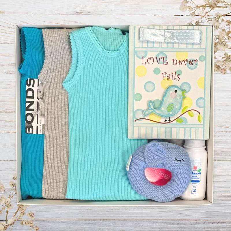 Baby gift set with boys clothes, an elephant blue toy, and a nursery plaque in a gift box on a wooden surface.