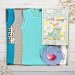 Baby gift set with boys clothes, an elephant blue toy, and a nursery plaque in a gift box on a wooden surface.