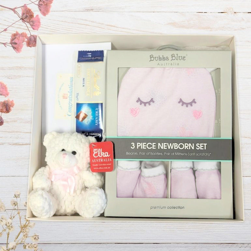 Baby gift set with teddy bear, booties, and hat in a box on a wooden surface.