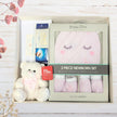 Baby gift set with teddy bear, booties, and hat in a box on a wooden surface.