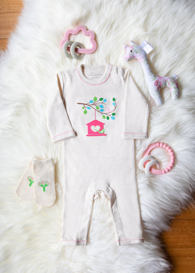 Baby outfit with onesie, mittens, and toys on a fluffy white surface