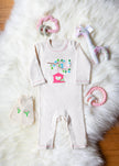 Baby outfit with onesie, mittens, and toys on a fluffy white surface
