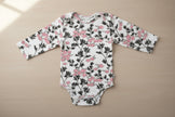 Floral-patterned baby onesie with long sleeves on a table background