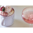 Mug with strawberry and cream dessert next to a glass of pink champagne on a white surface