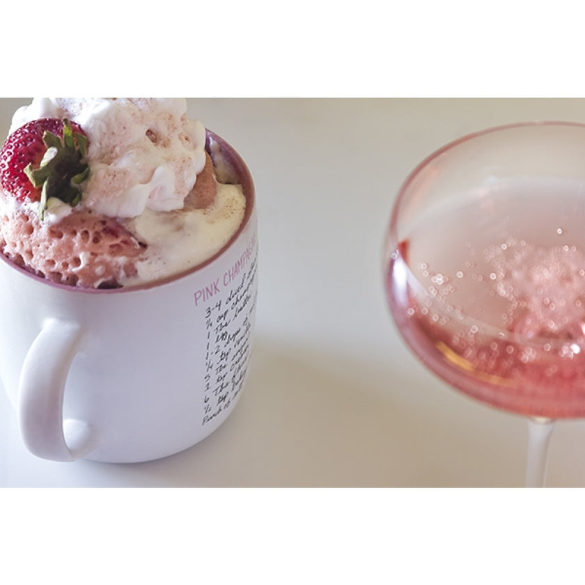 Mug with strawberry and cream dessert next to a glass of pink champagne on a white surface