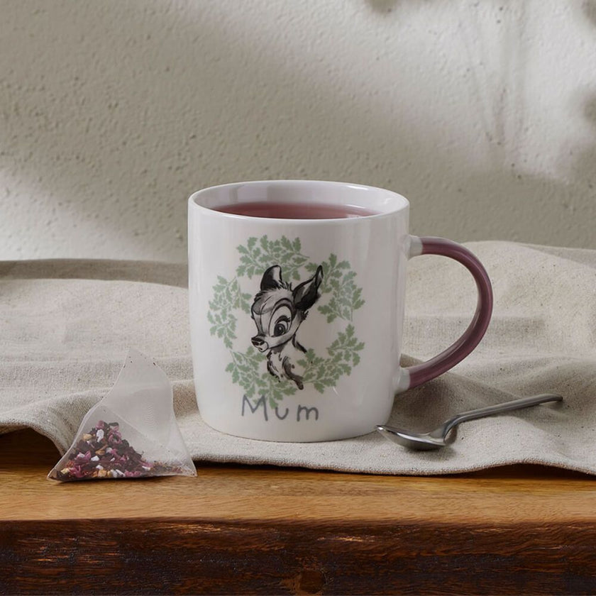 White mug with Bambi design and 'Mum' text on a wooden surface with a tea bag and spoon.