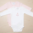 Two baby bodysuits, one pink and one white, on a table background
