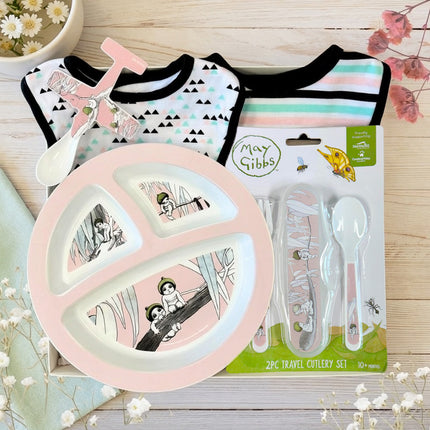 May Gibbs themed baby gift set with Gumnut Babies pink plate, cutlery, and bibs on a wooden surface.