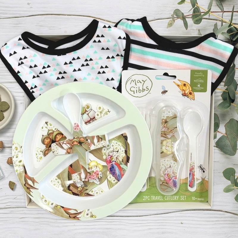 Gift set with May Gibbs plate, cutlery and baby bibs in a box on a wooden surface.