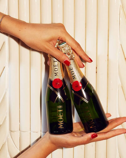 Two Moët champagne bottles held by a hand against a light background