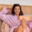 Woman in a pink robe holding a 'Mum Power' card on a couch.