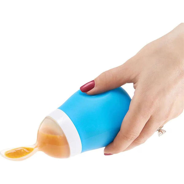 Hand holding a blue baby spoon with a white cap, filled with orange liquid.