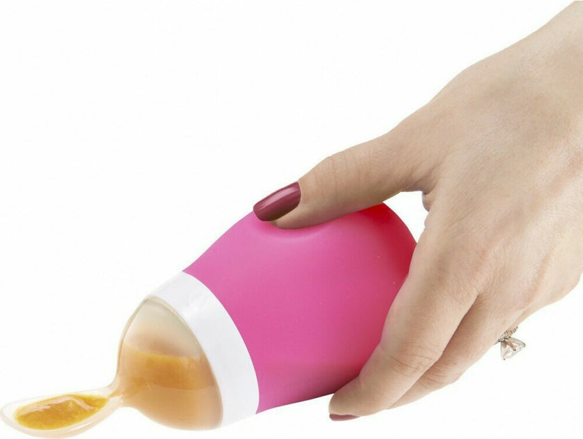 Pink silicone spoon with a white rim being held by a hand on a white background
