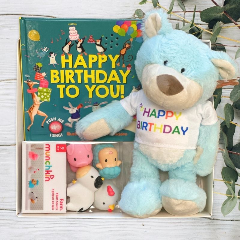 Blue teddy bear with 'Happy Birthday' shirt and children's book in a gift box