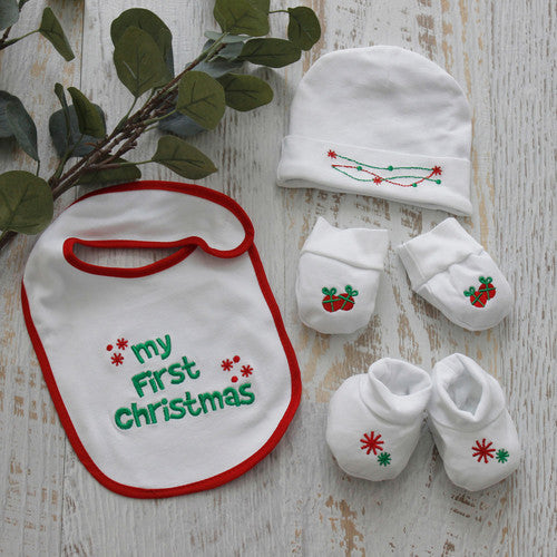 Baby gift set with bib, hat, and booties on a wooden surface with greenery.