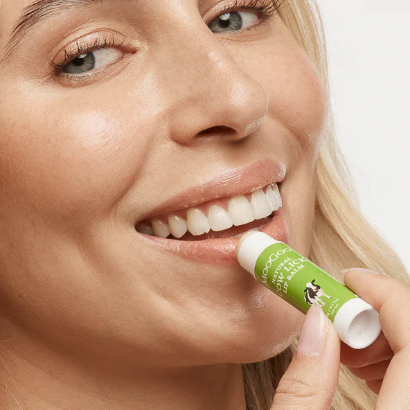 Woman applying a green lip balm to her lips with a white background