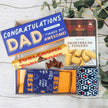 Collection of dad gifts including a box of shortbread fingers, Toblerone chocolate, and a drink cooler, gift box by 'The Baby Gift Company'.